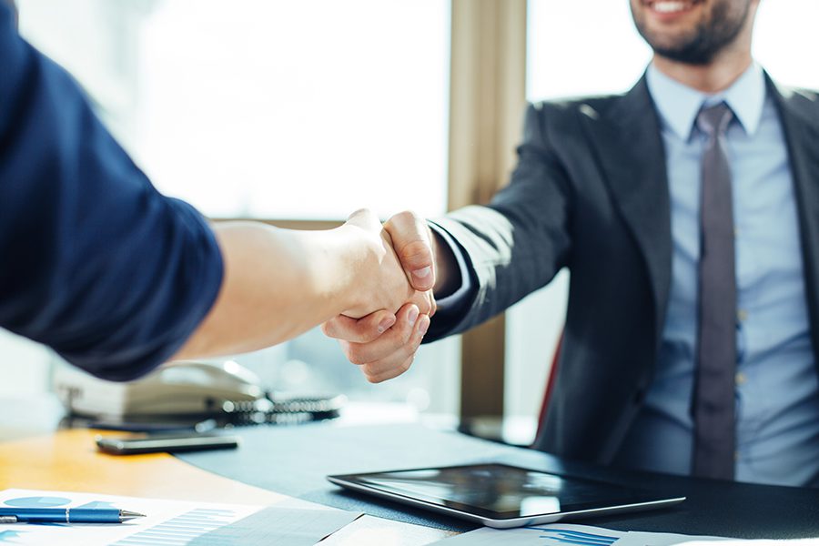 About Our Agency - Bright Image of Two Businessmen Shaking Hands in an Office in Front of Large Window